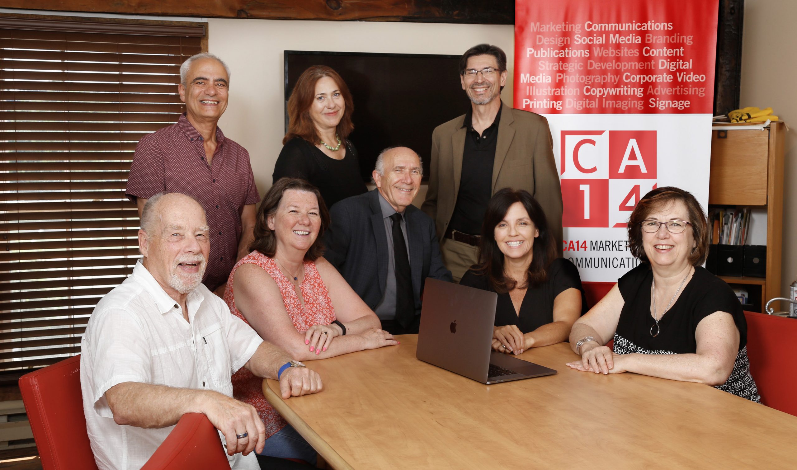 CA14 team sitting at a board table with a screen behind them on the wall and a pull up marketing banner on display.
